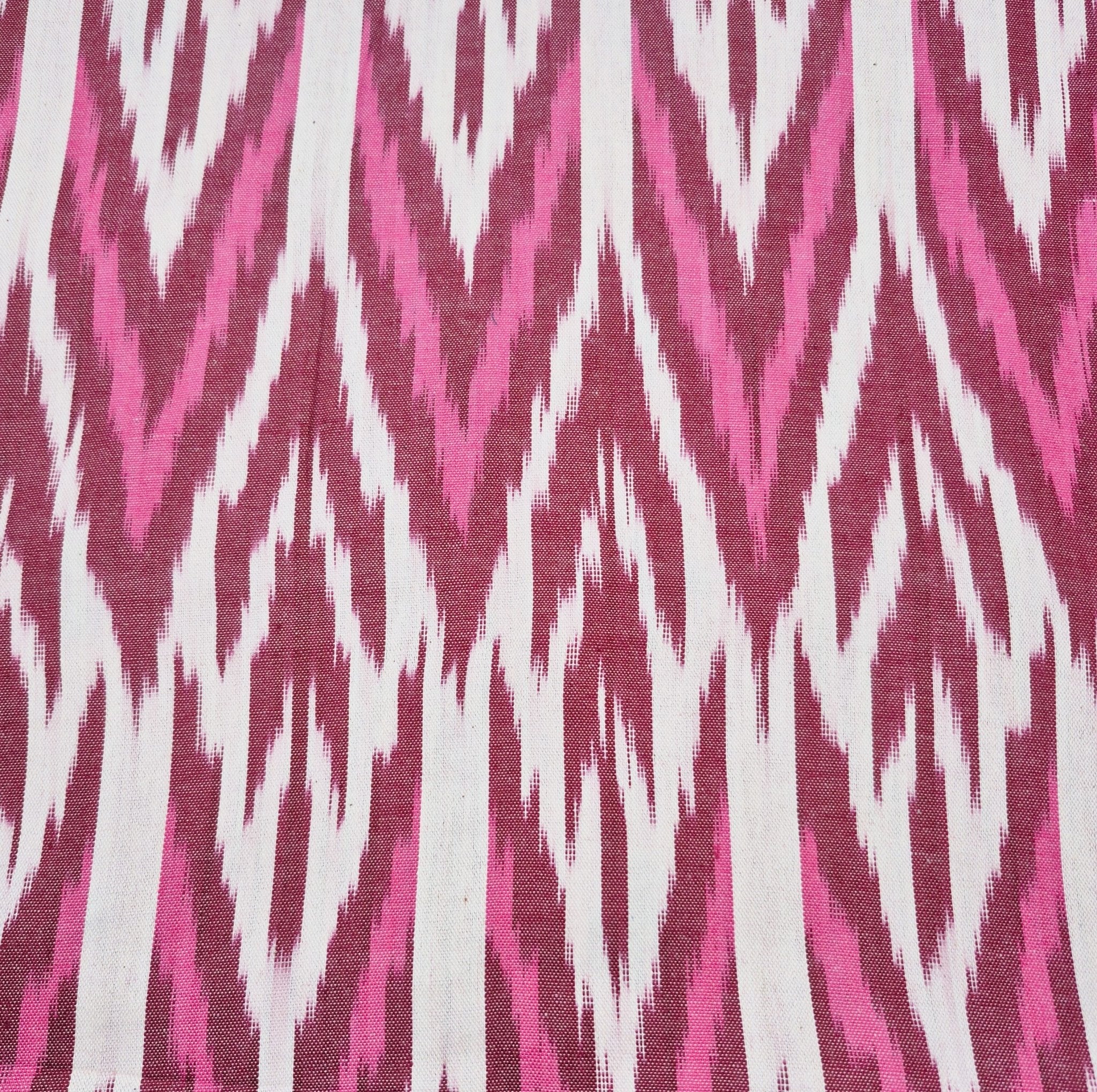 Reverse side of the burgundy ikat table runner, showing the pink woven fabric with burgundy thread.
