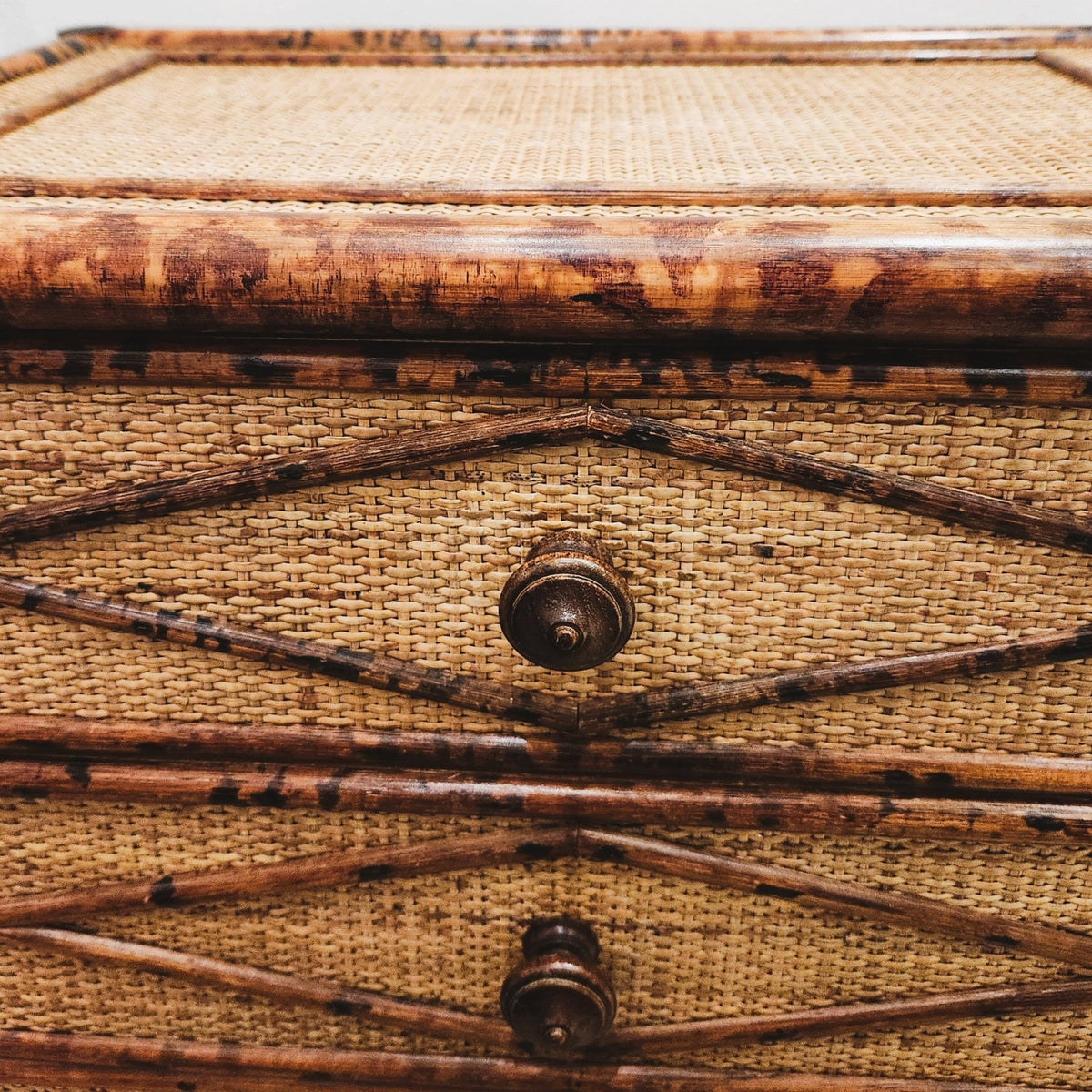 Close view of the diamond-patterned tortoiseshell bamboo trim over the cane-wrapped wooden base of the chest