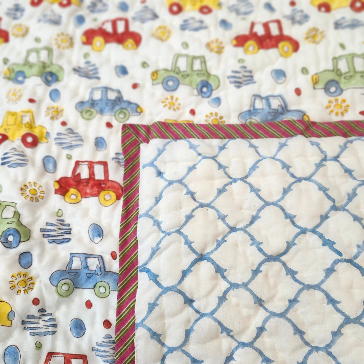 Child's block print quilt with a colourful car design on one side and a blue trellis pattern on the other