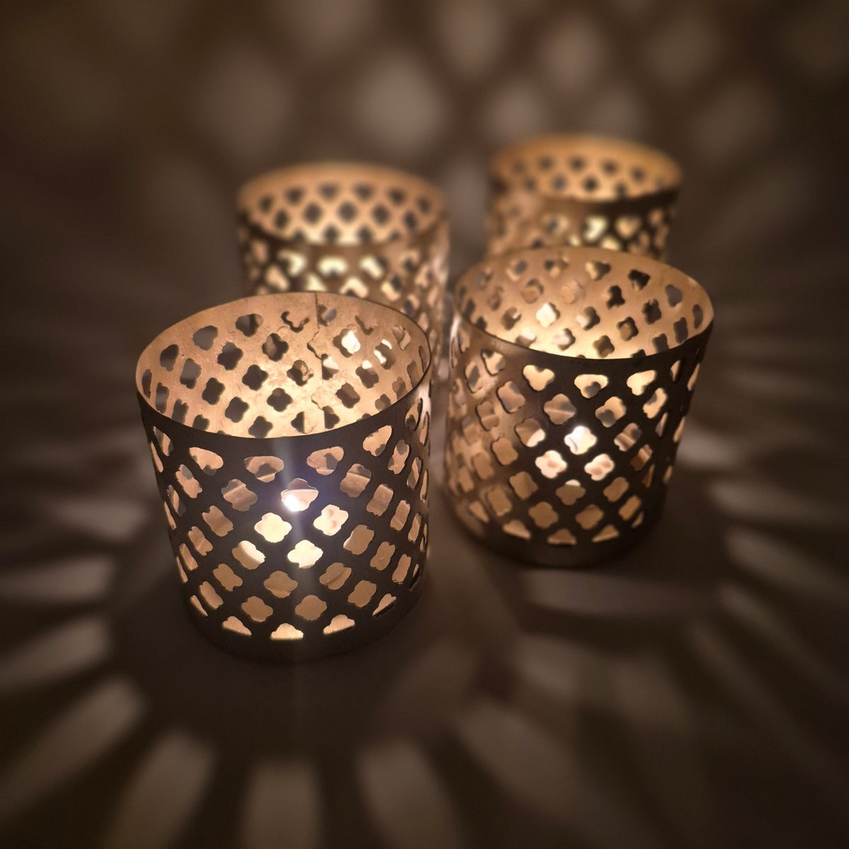 Gold painted iron tea light holder with fret-work sides, 9 cm high and 9 cm in diameter, casting a patterned light