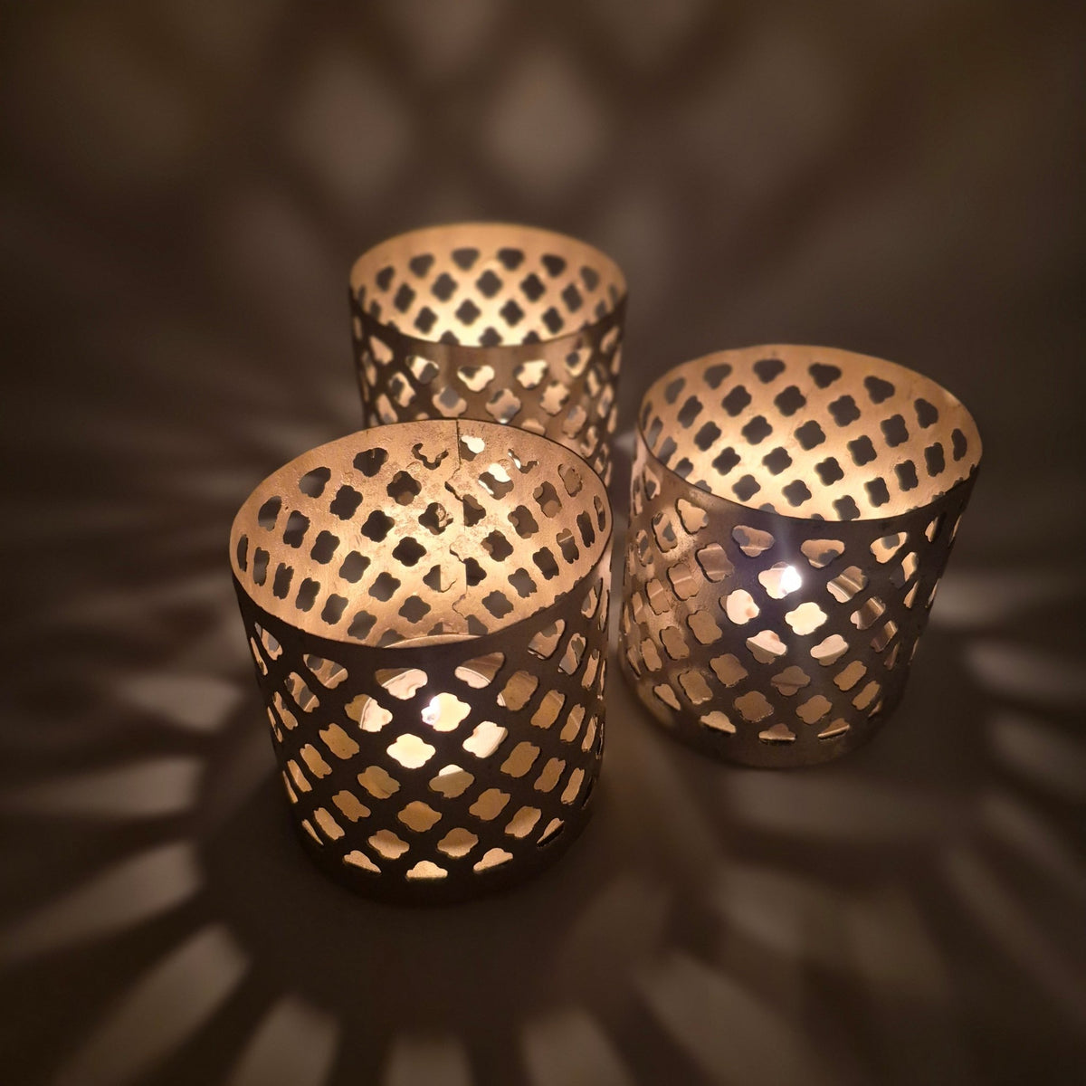 Fret-work iron tea light holder painted gold, 9 cm tall and 9 cm across, with pierced sides that scatter candlelight
