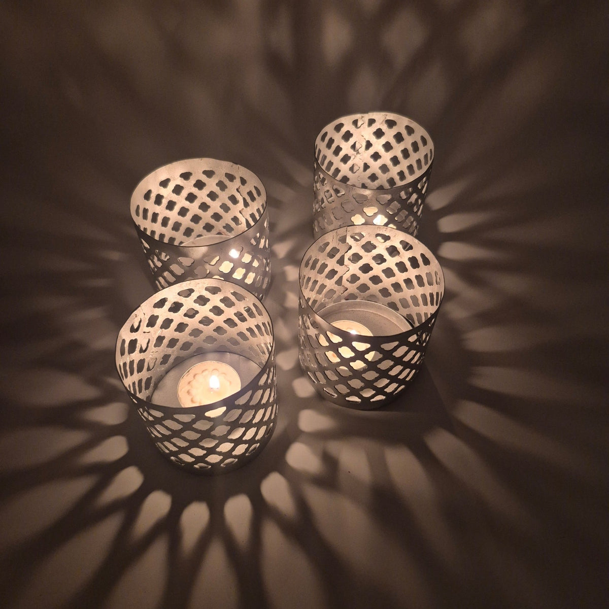 Fret-work iron tea light holder painted silver, 9 cm tall and 9 cm across, with pierced sides that scatter candlelight