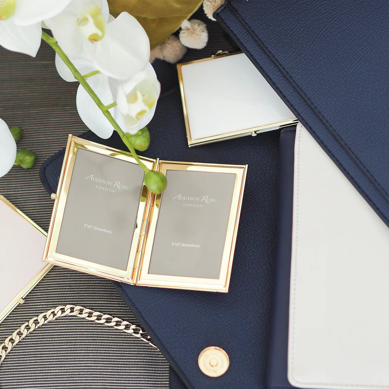 White enamel and gold-plated travel photo frame holding two 2 x 3 inch photos, with a velvet drawstring pouch