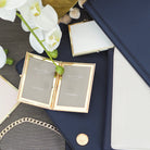 White enamel and gold-plated travel photo frame holding two 2 x 3 inch photos, with a velvet drawstring pouch